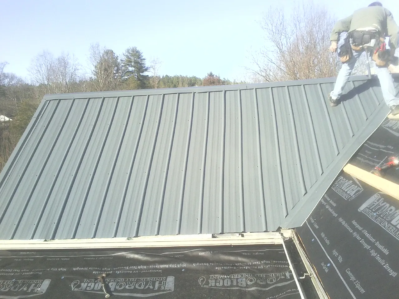 Crew installing dark green standing seam panels over synthetic underlayment in Willow Wood
