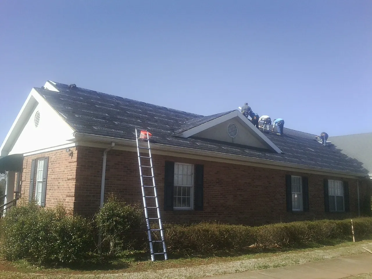 Crew tearing shingles off a brick ranch roof with a ladder set — Metal Roof Repair work by our crew in Willow Wood
