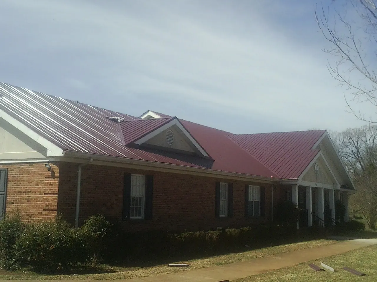 Red metal roof with gabled entries on a long brick building, from a Hail Damage Roof Repair job in Willow Wood