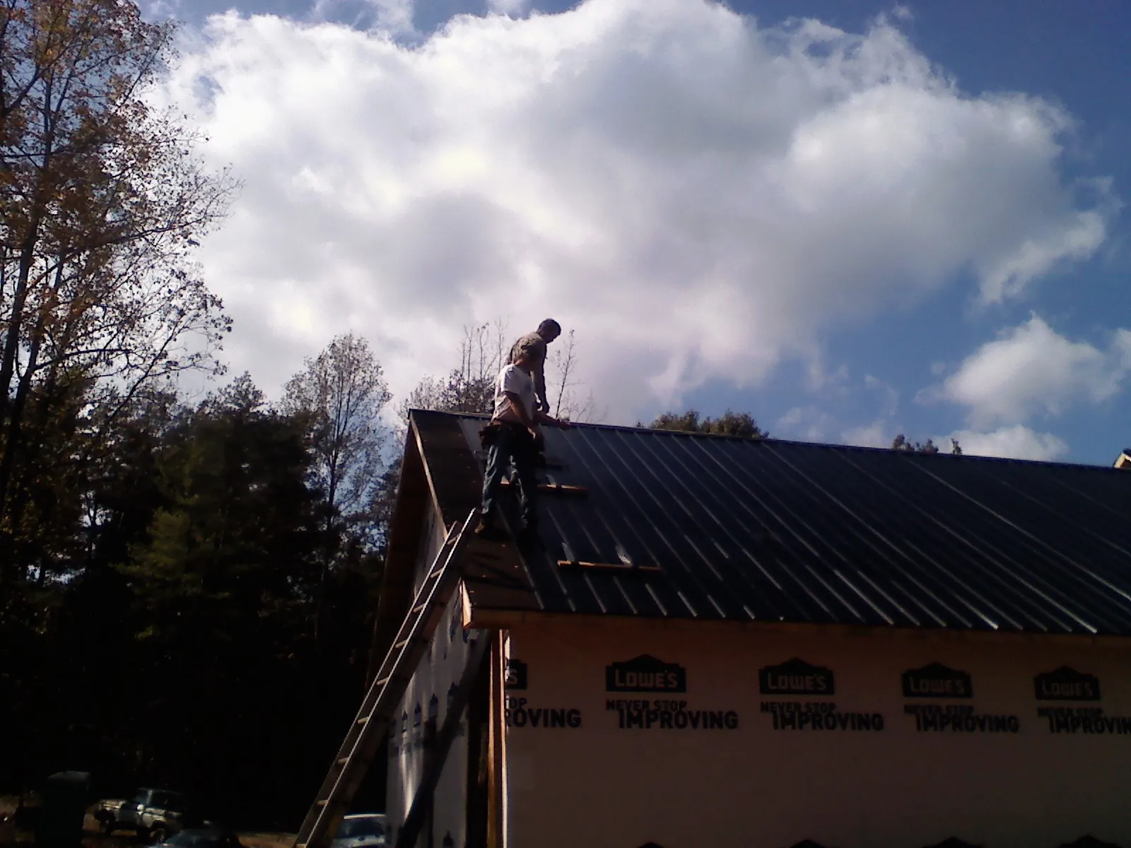 Roofer fastening dark metal panels high against a cloudy sky, from a Roof Inspection job in Willow Wood
