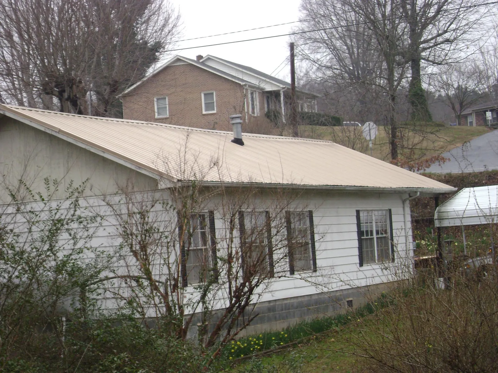 Tan metal roof on a white sided house set into a hillside — Commercial Roofing by Roofing Brothers in Willow Wood