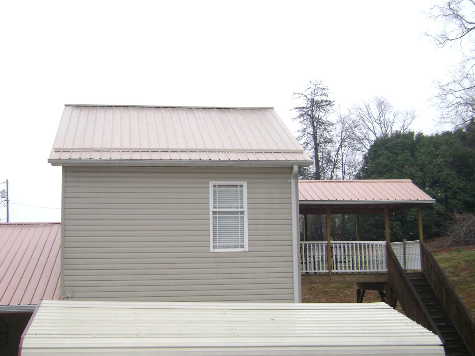 Tan metal roofs on a two story addition and attached porch, from a Roof Replacement job in Willow Wood